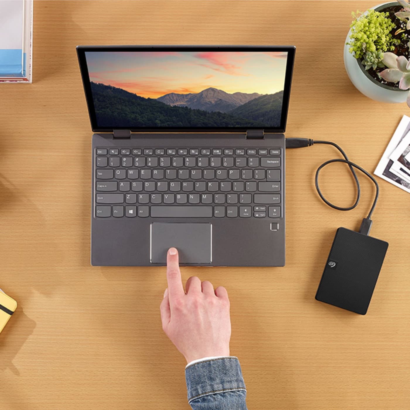 Seagate Expansion Portable hard drive plugged into a laptop on a wooden desk.